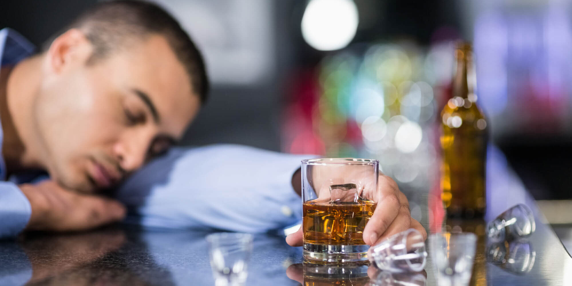 Man asleep at bar drinking whiskey to illustrate use of alcohol as a dysfunctional coping mode used to distract and numb feelings that people do not wish to deal with.