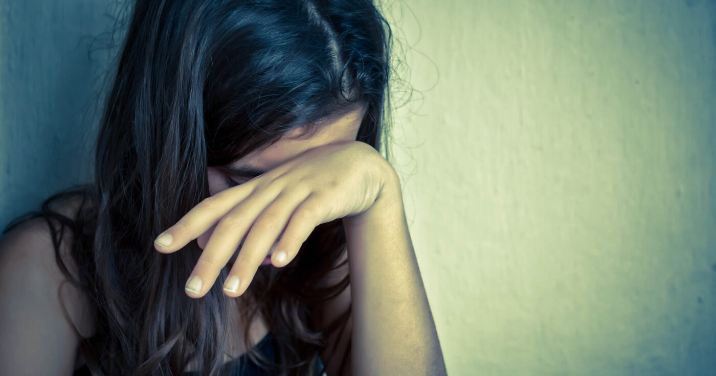 Image of a girl covering her face with hand representing a sad, lonely child with unmet emotional needs